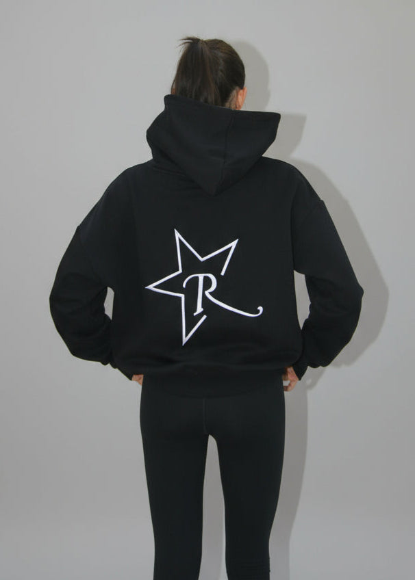 Person wearing a black hoodie with a logo on the back, standing against a white backdrop.