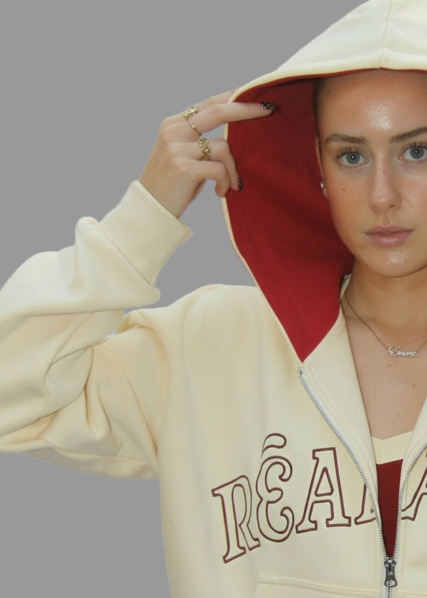 Person wearing a beige hoodie with red lining and 'Réalité' branding on a plain background